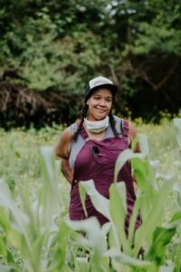 an image of a Black femme farmer standing in a field of grass and corn plants